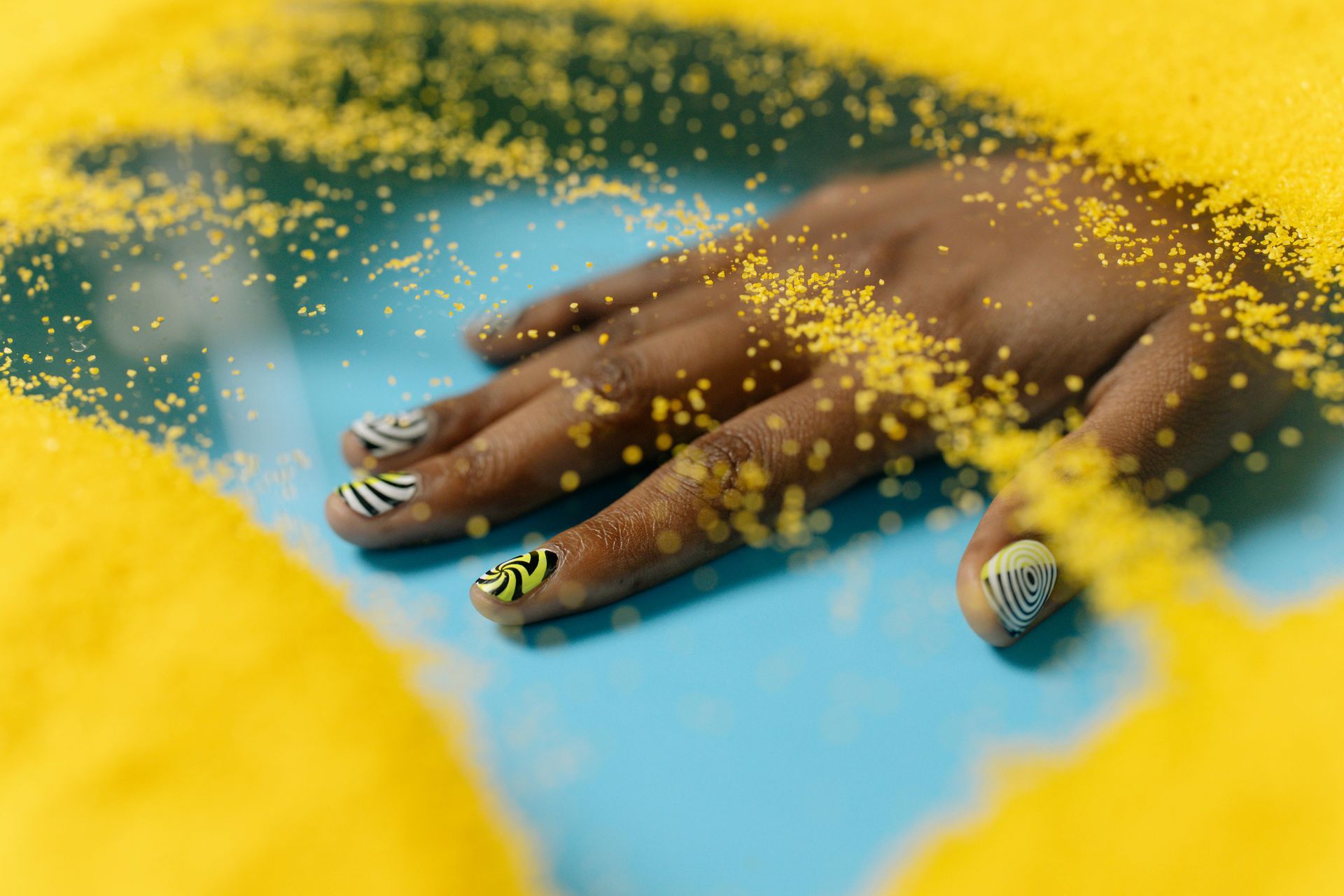 Hand with zebra-print nails submerged in yellow material, resting on a blue surface.