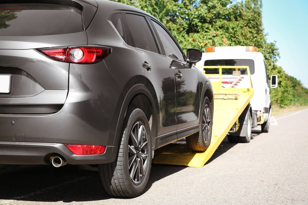 A Dark Gray SUV Being Loaded Onto a Flatbed Tow Truck on a Road Near Trees — Penfold Towing in Dundowran Beach, QLD