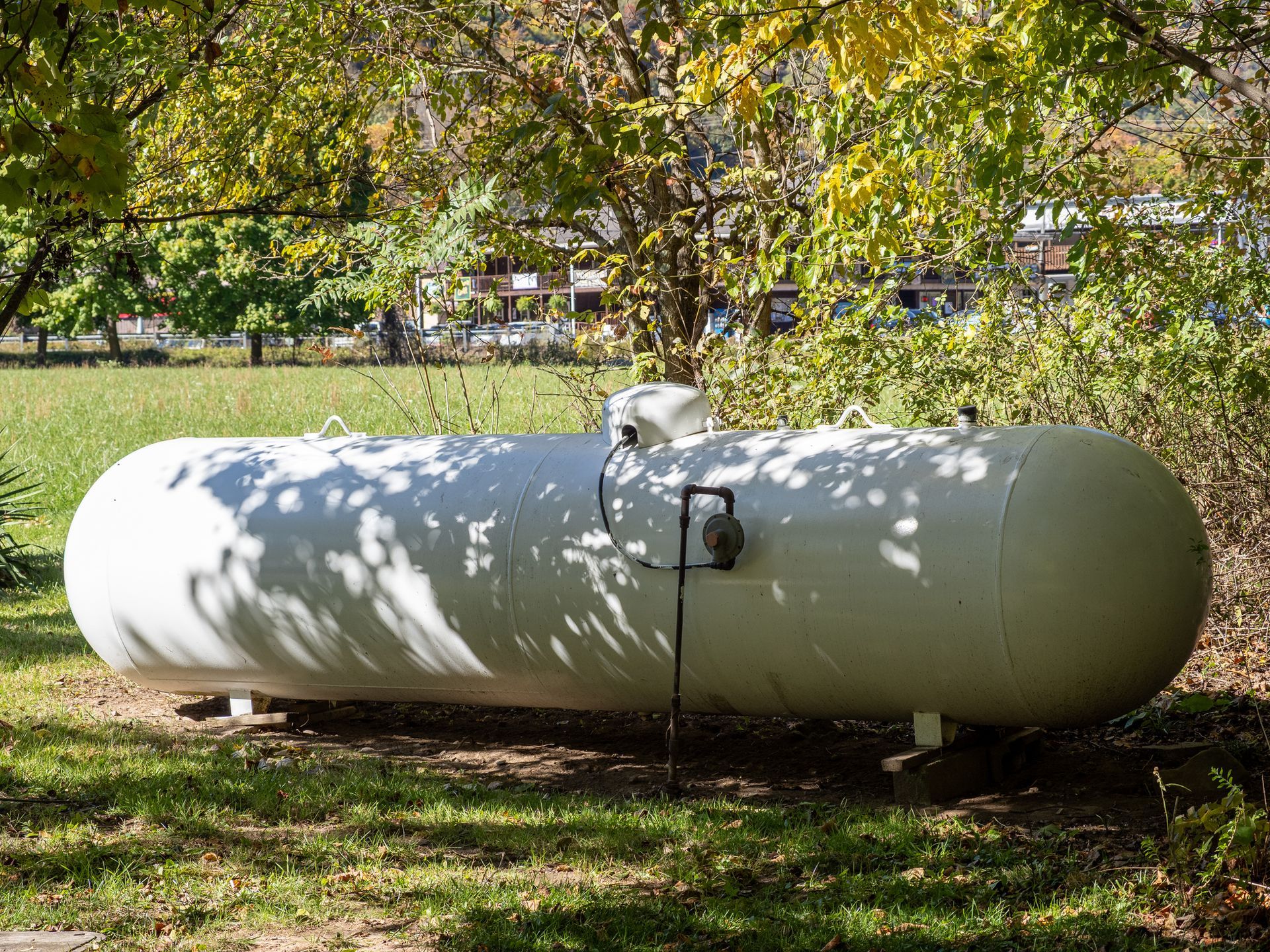 A large white propane tank is sitting in the grass.
