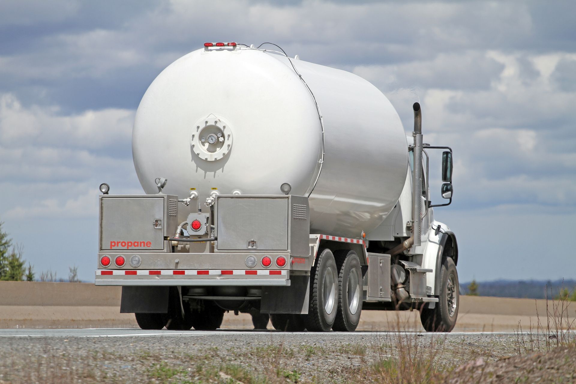 A white tanker truck is driving down the road.