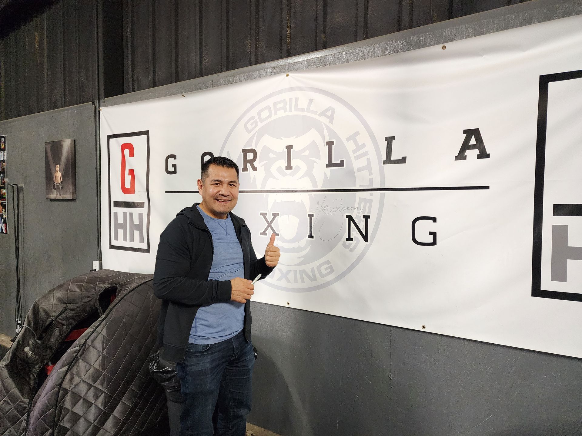 Man posing with a thumbs-up beside a Gorilla Boxing banner and gym logo