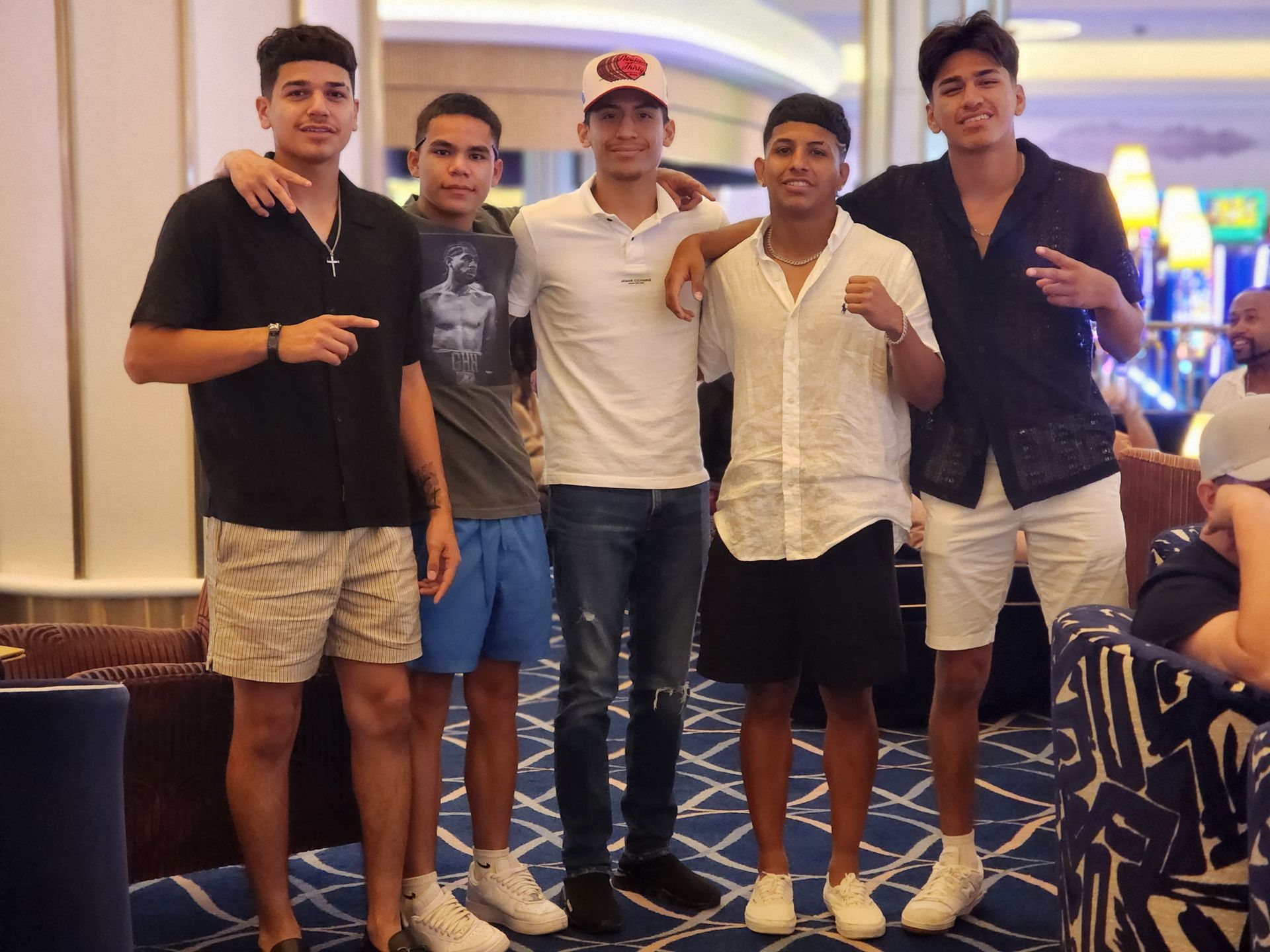Five people posing indoors, with one man in a white cap centered among them.