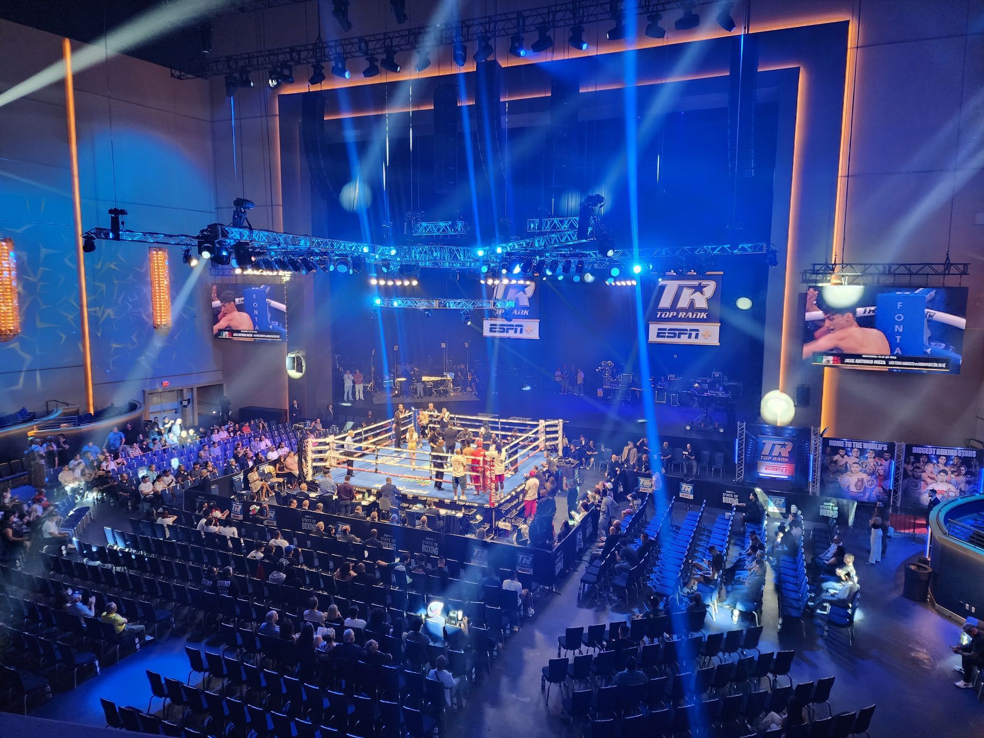 Blue-lit esports arena with a large stage, giant screens, and a seated audience during a live competition