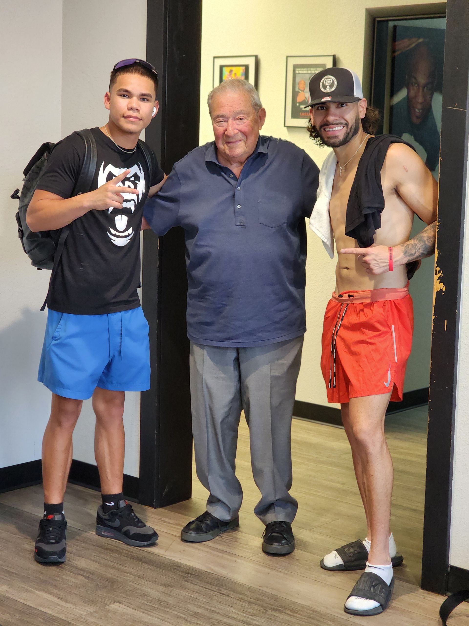 Three men standing indoors, smiling and posing together in casual clothes.