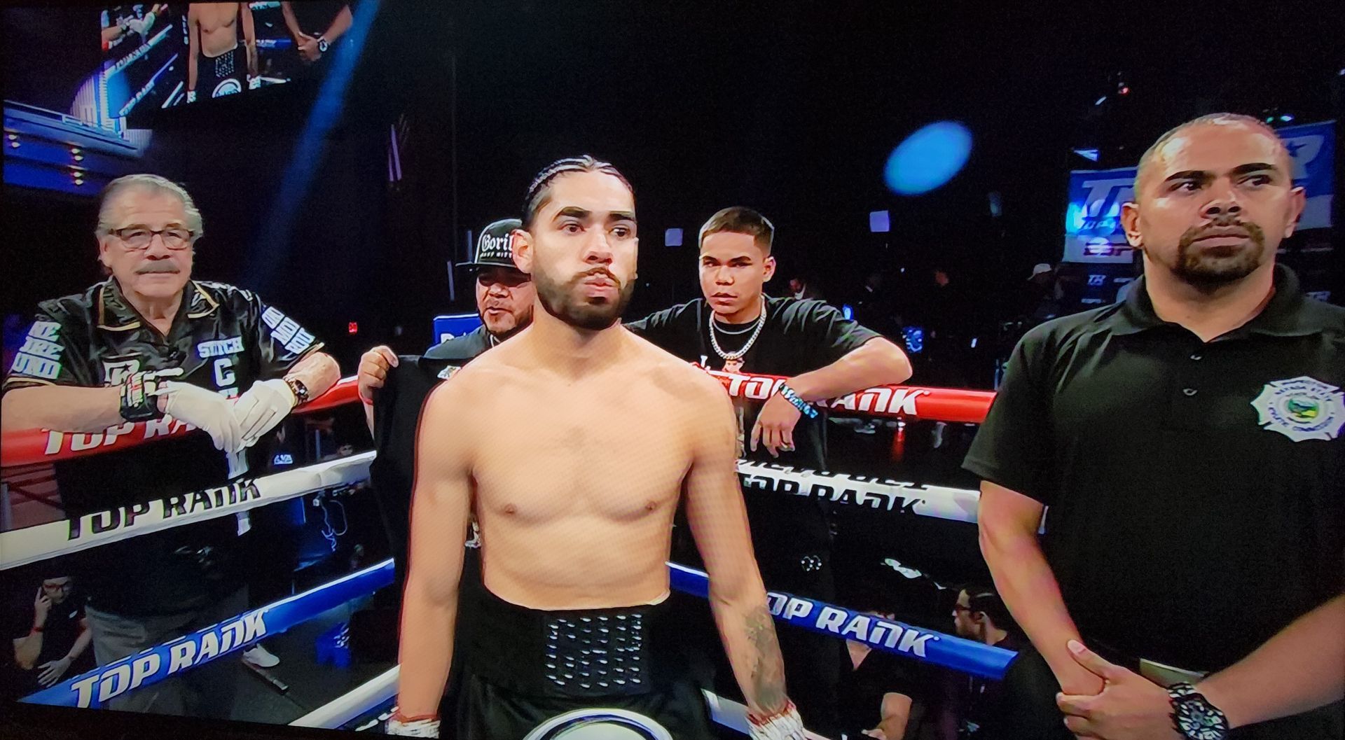 Boxer standing in a ring with two cornermen behind him, focused before a fight