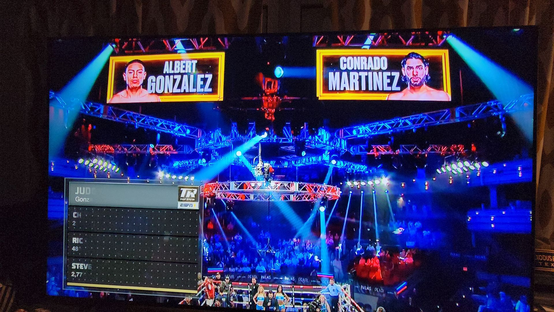 Boxing arena with bright blue lights and giant screens showing Gonzales vs. Martinez