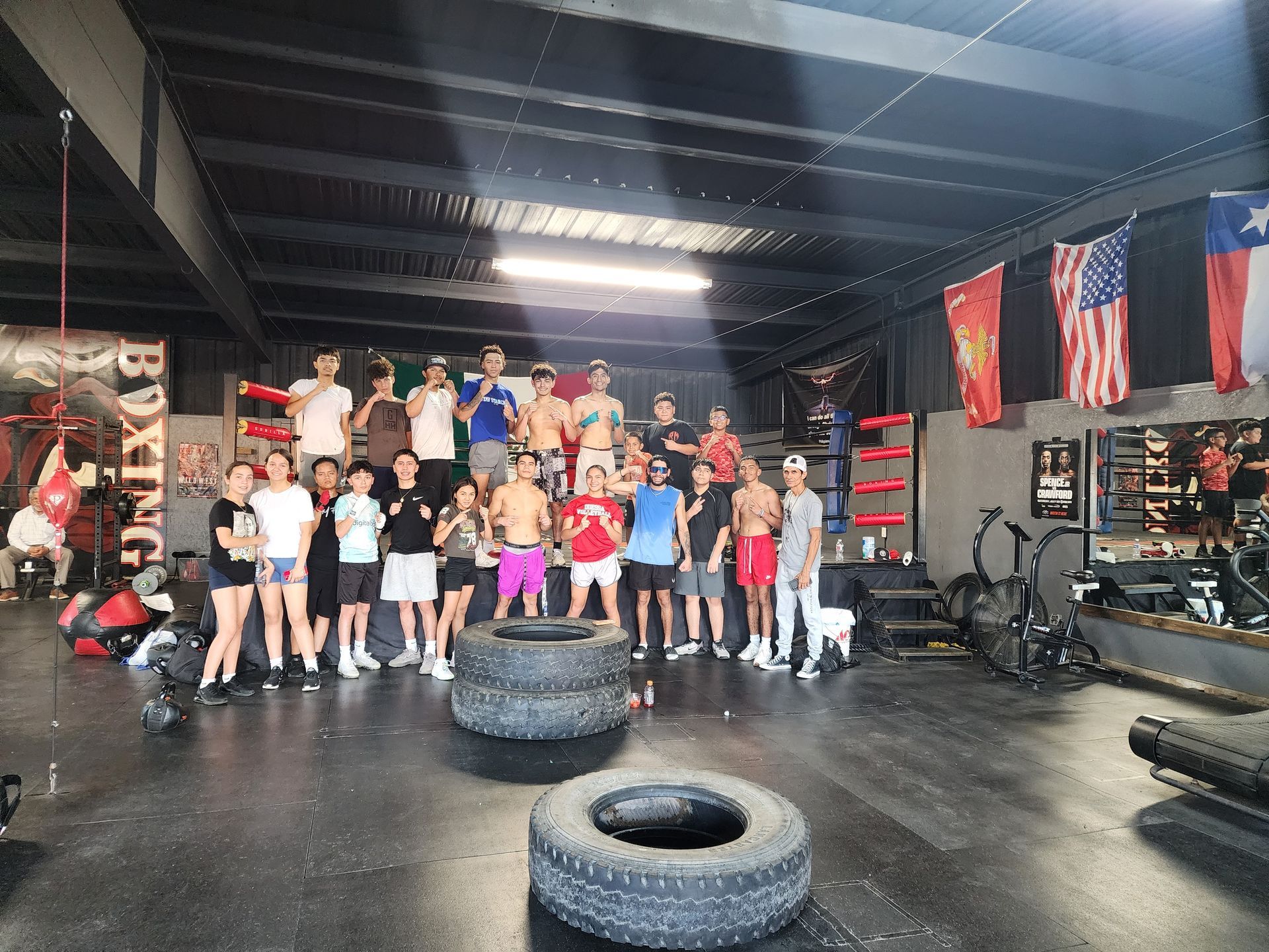 Group posing in a gym with tires, pull-up rigs, and hanging flags.