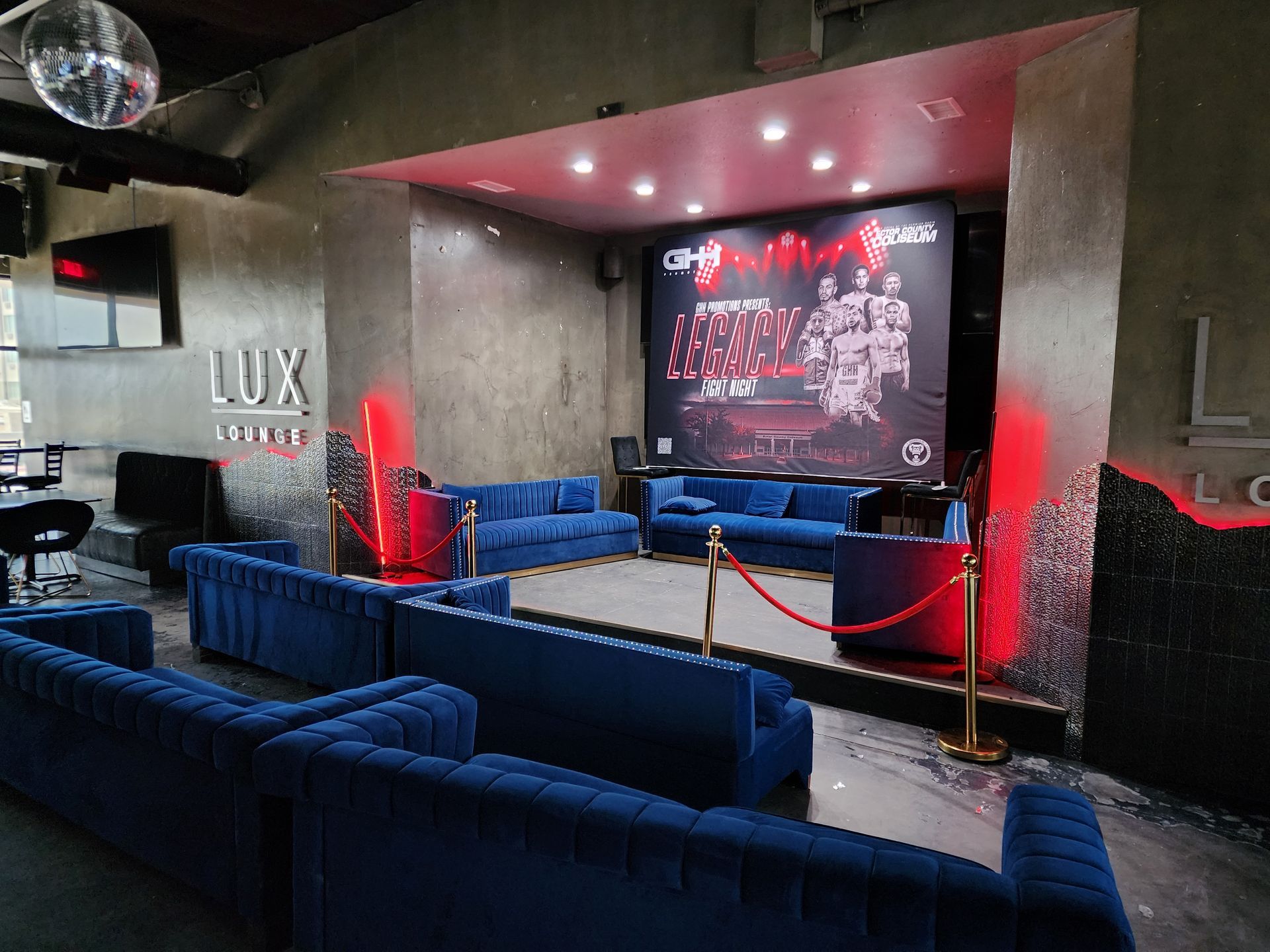 Dim lounge with blue sofas, red velvet ropes, and a neon-lit stage-like wall mural