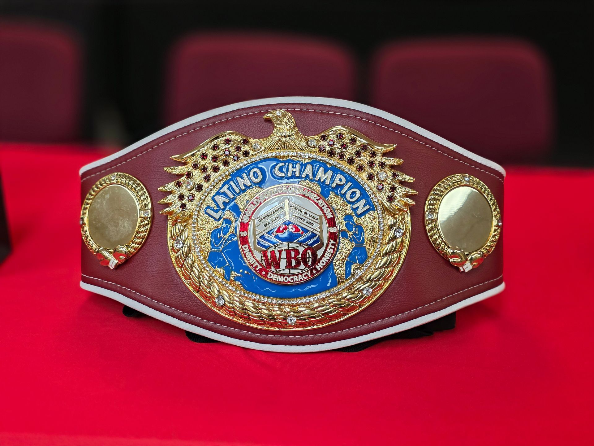 A gold championship belt with blue center plate resting on a red tablecloth in an auditorium