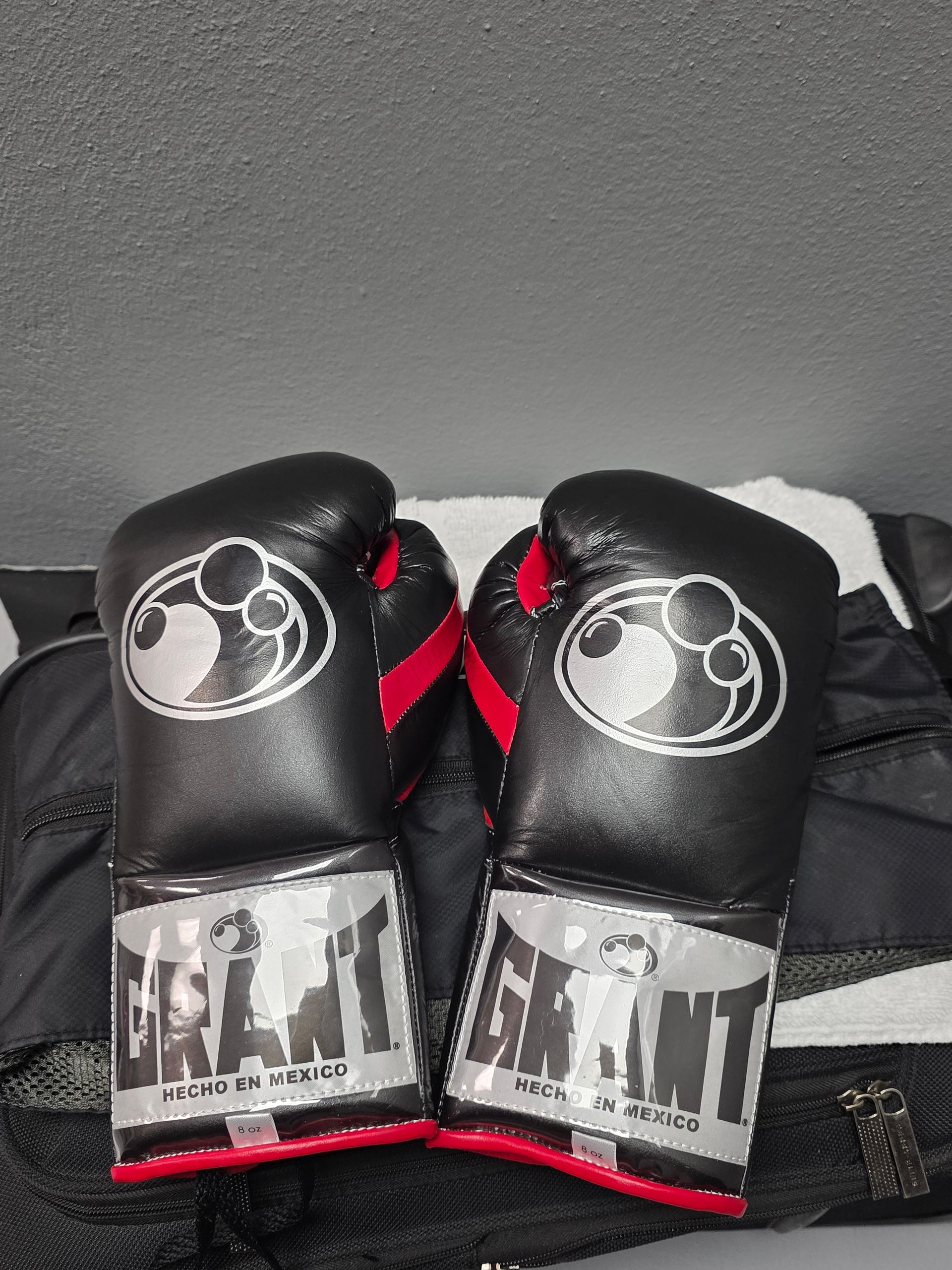 Pair of black boxing gloves with white logos and red accents, resting on a dark surface.