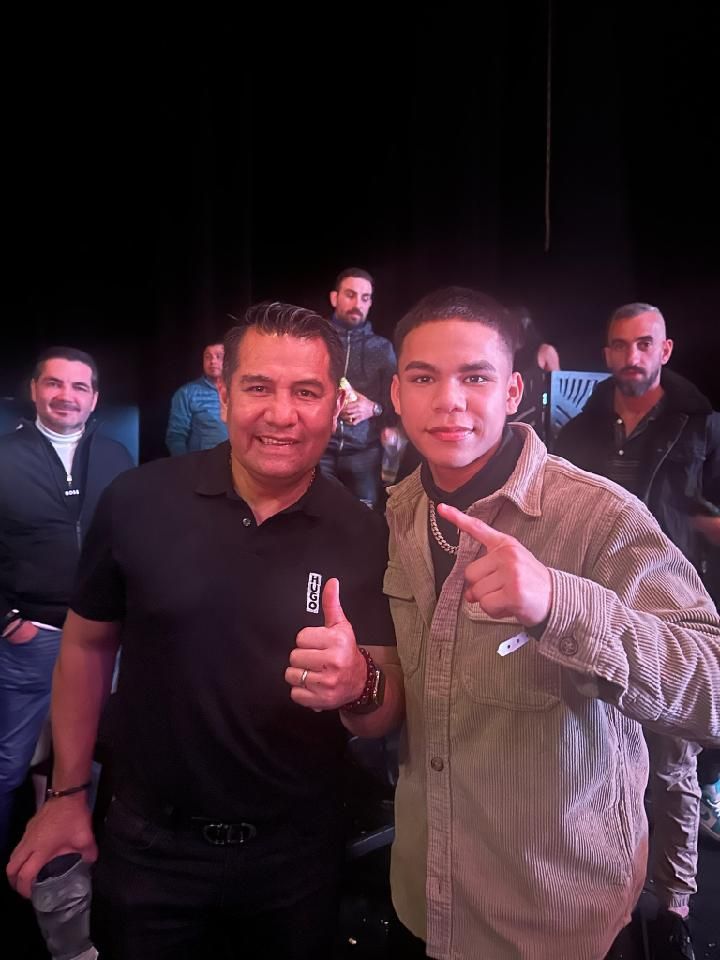 Two people posing with thumbs up at a dimly lit event, with others in the background.