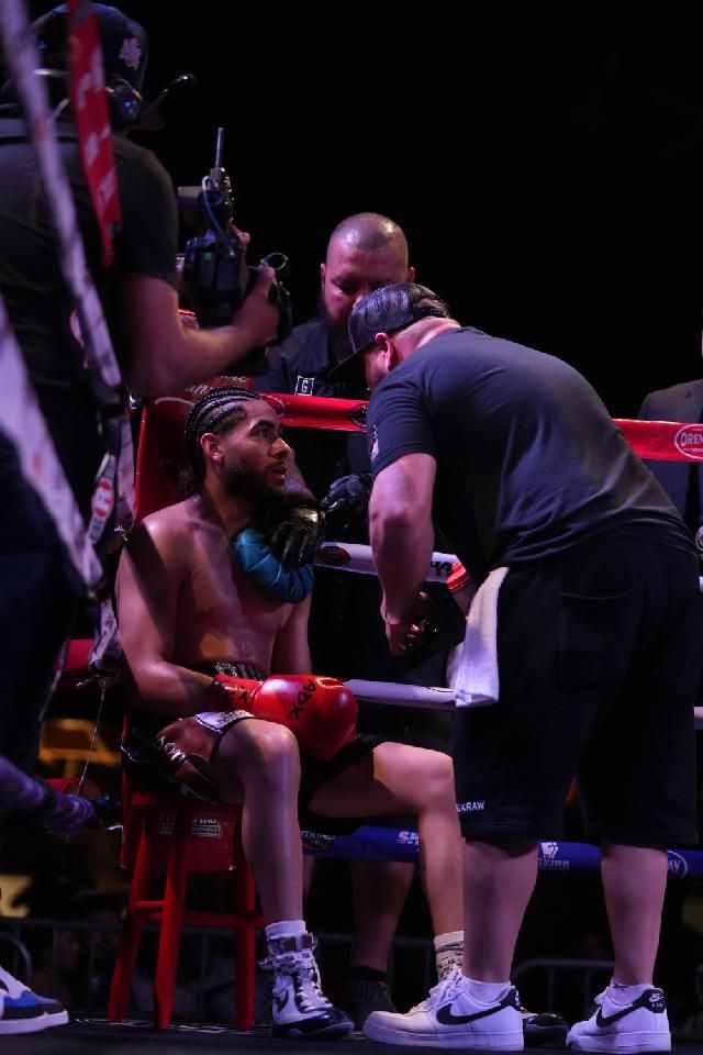 Boxer seated in corner of the ring as coach and referee check on him during a match