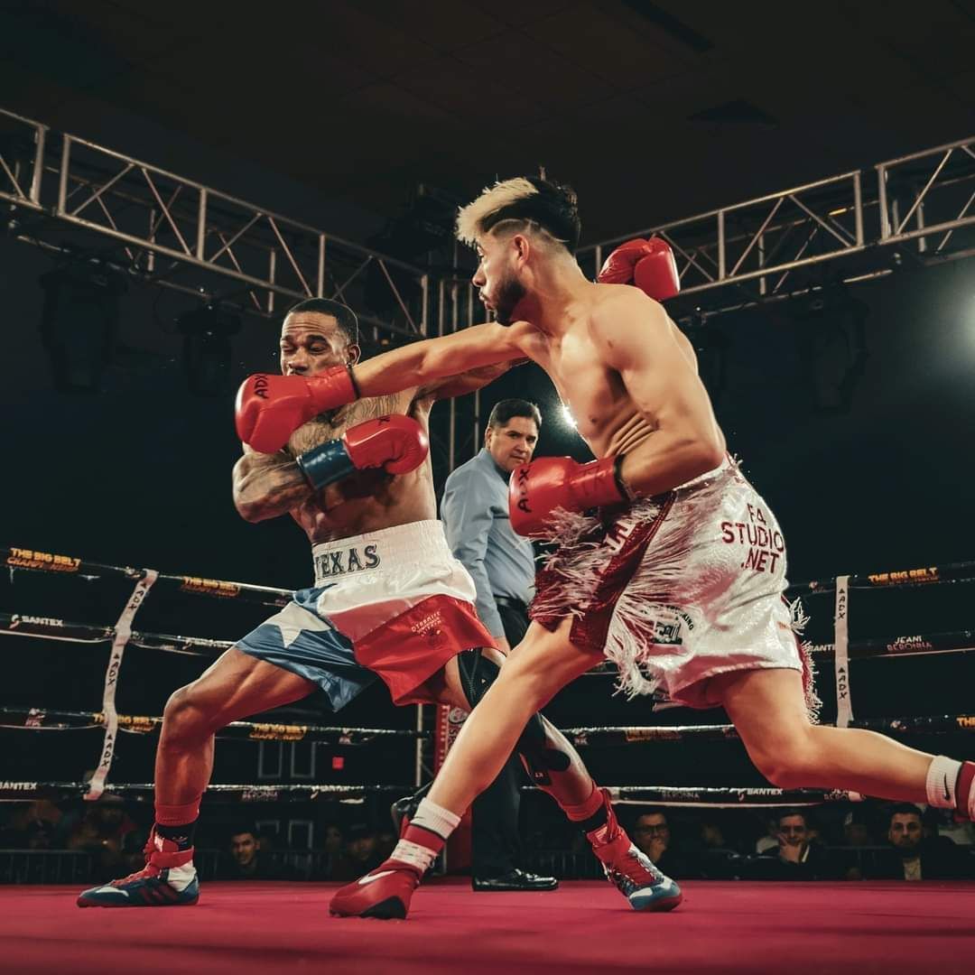 Two boxers in red gloves sparring in a boxing ring under arena lights