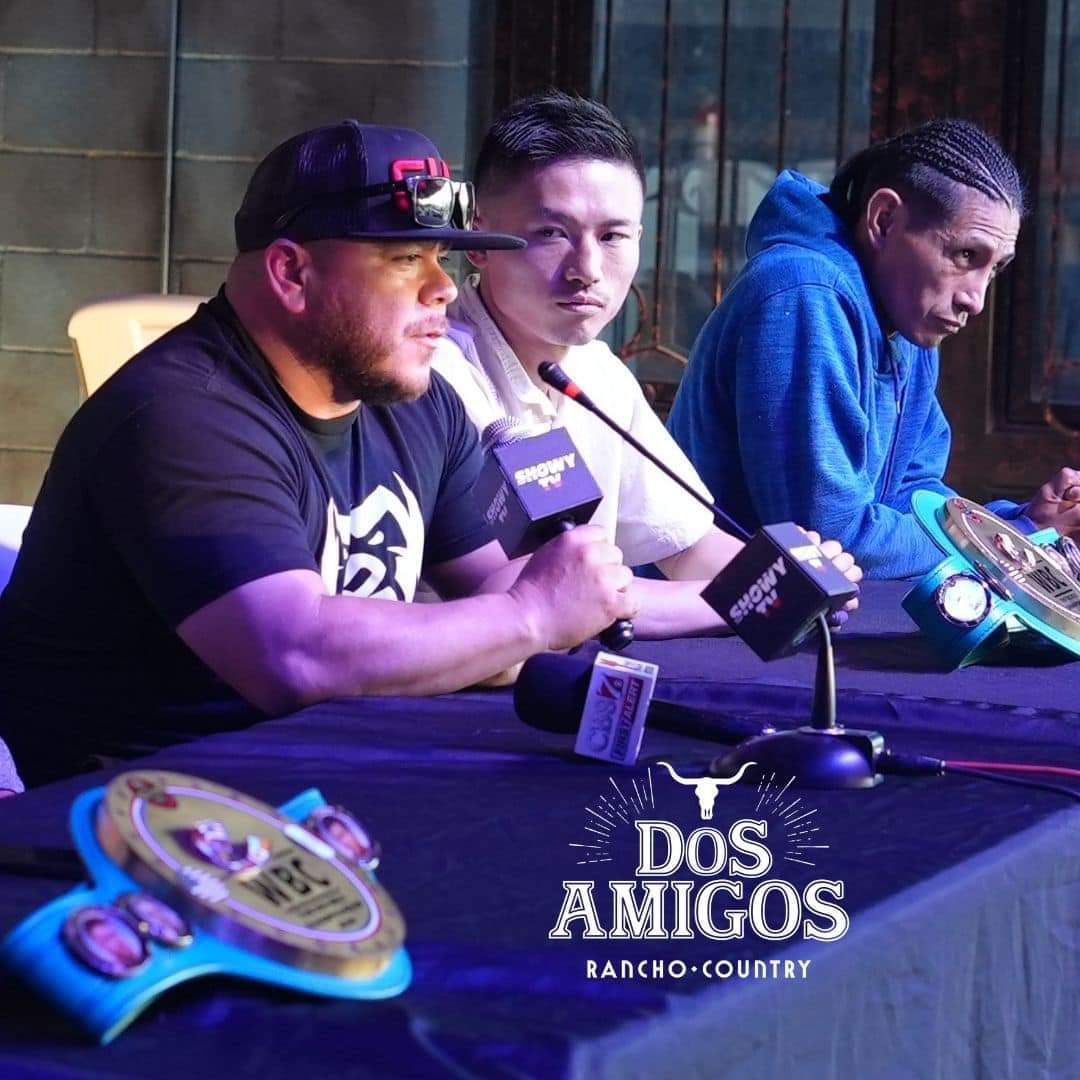 Three men seated at a podcast table with microphones and a Dos Amigos sign in a dim studio.