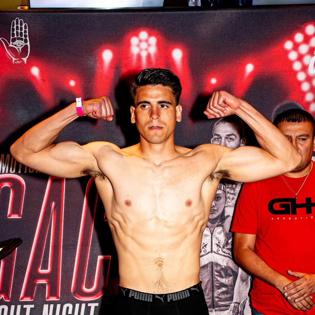 Boxer posing with flexed arms on stage in front of a red-lit backdrop