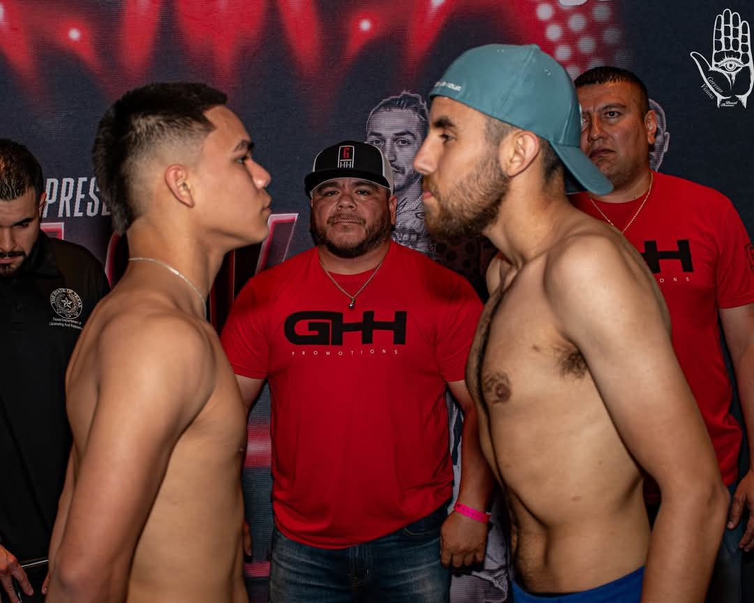 Two shirtless fighters face off at weigh-in with an official behind them.