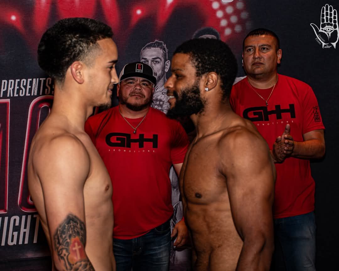 Two shirtless fighters face off at a weigh-in with officials behind them under red lighting.