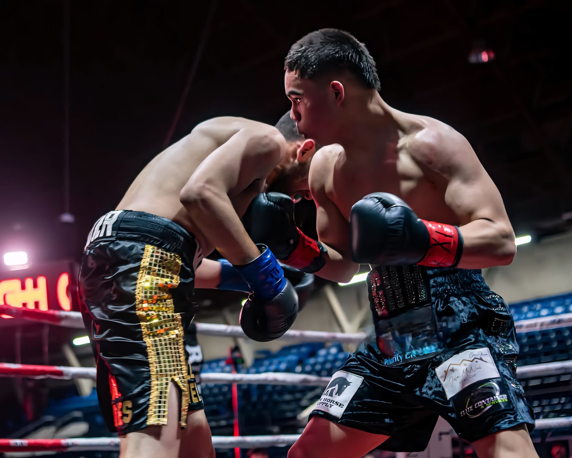 Two boxers trading punches in a ring, one in black and gold shorts, under bright arena lights