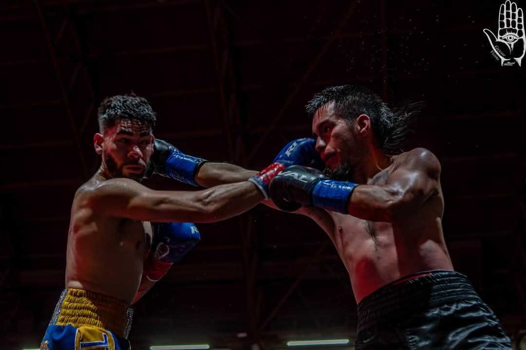 Two boxers in a ring exchange punches, wearing blue gloves under dramatic red lighting.