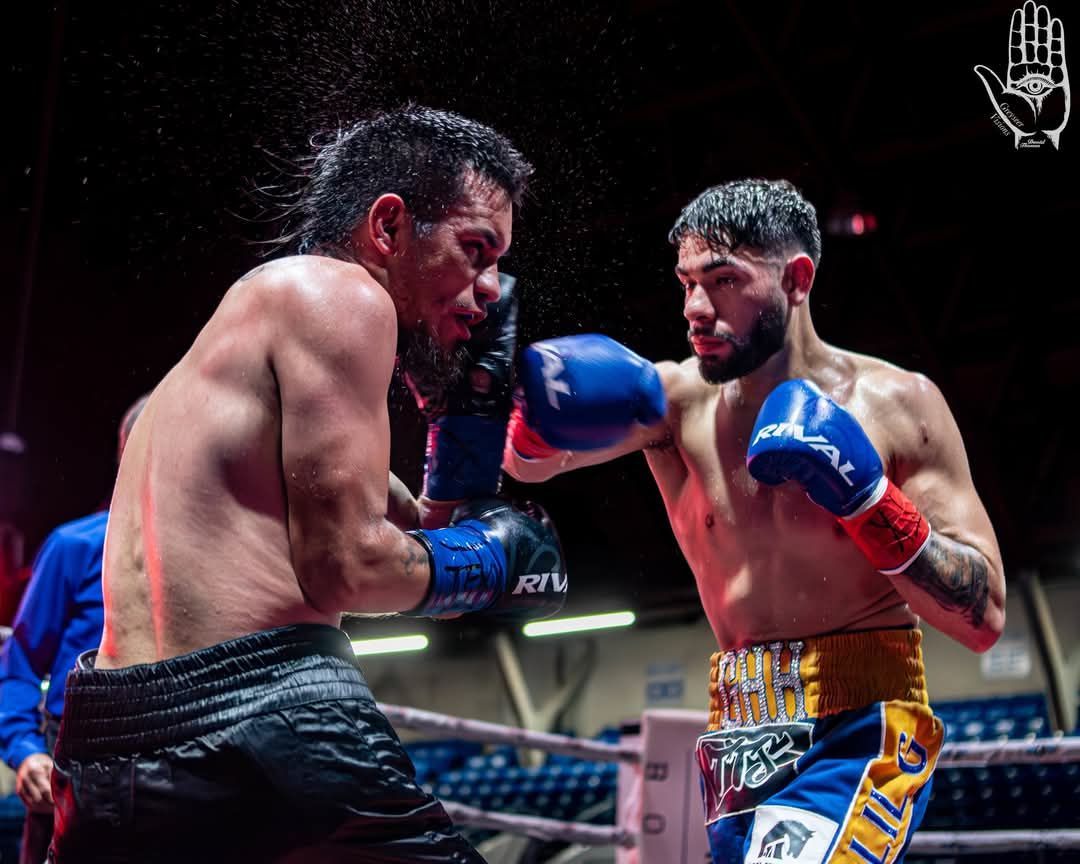 Two boxers in a ring exchanging punches, one in blue gloves and gold trunks, under bright arena lights