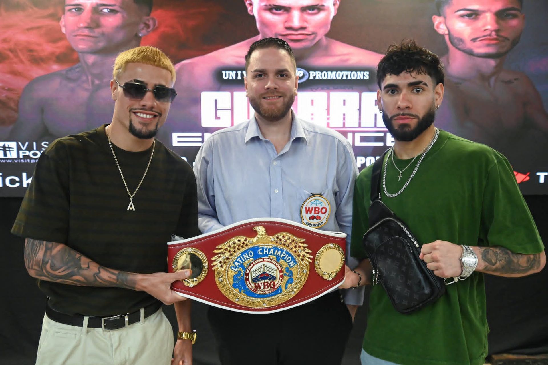 Three men pose with a championship boxing belt in front of a fight promotion backdrop.