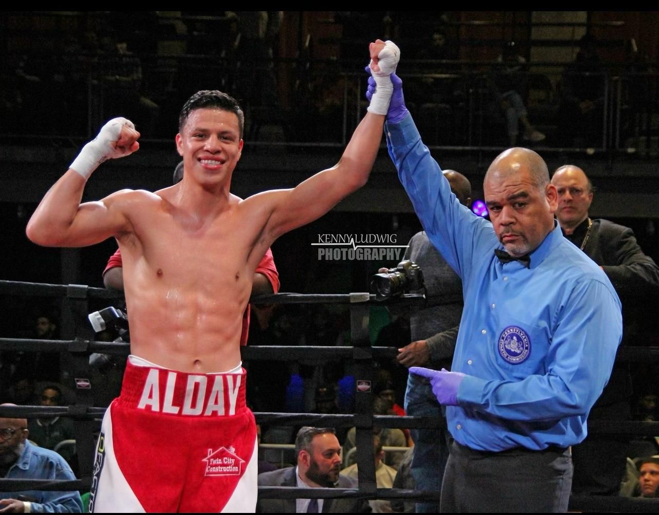 Boxer in red shorts celebrates as referee raises his arm in the ring after a match.