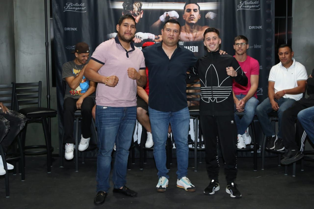 Three people posing indoors at an event, with seated attendees and a dark backdrop behind them.