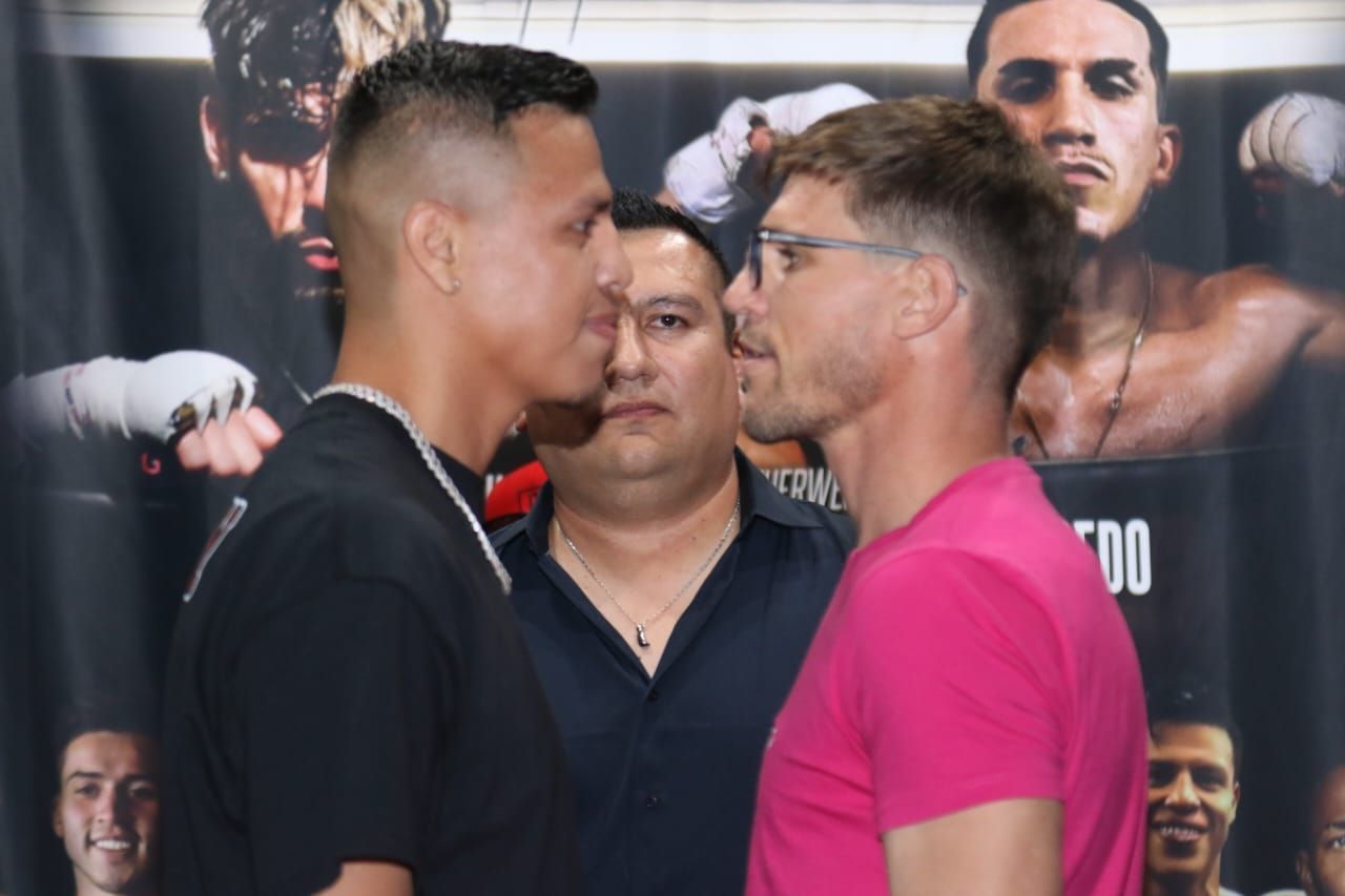 Two men face off nose-to-nose at a boxing weigh-in, with a man standing between them.