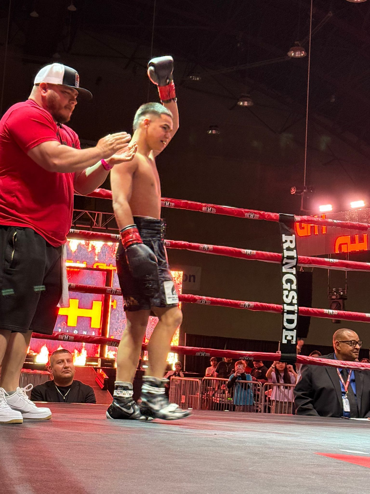 Boxing ring: trainer steadies a red-clad fighter while officials stand nearby under bright lights