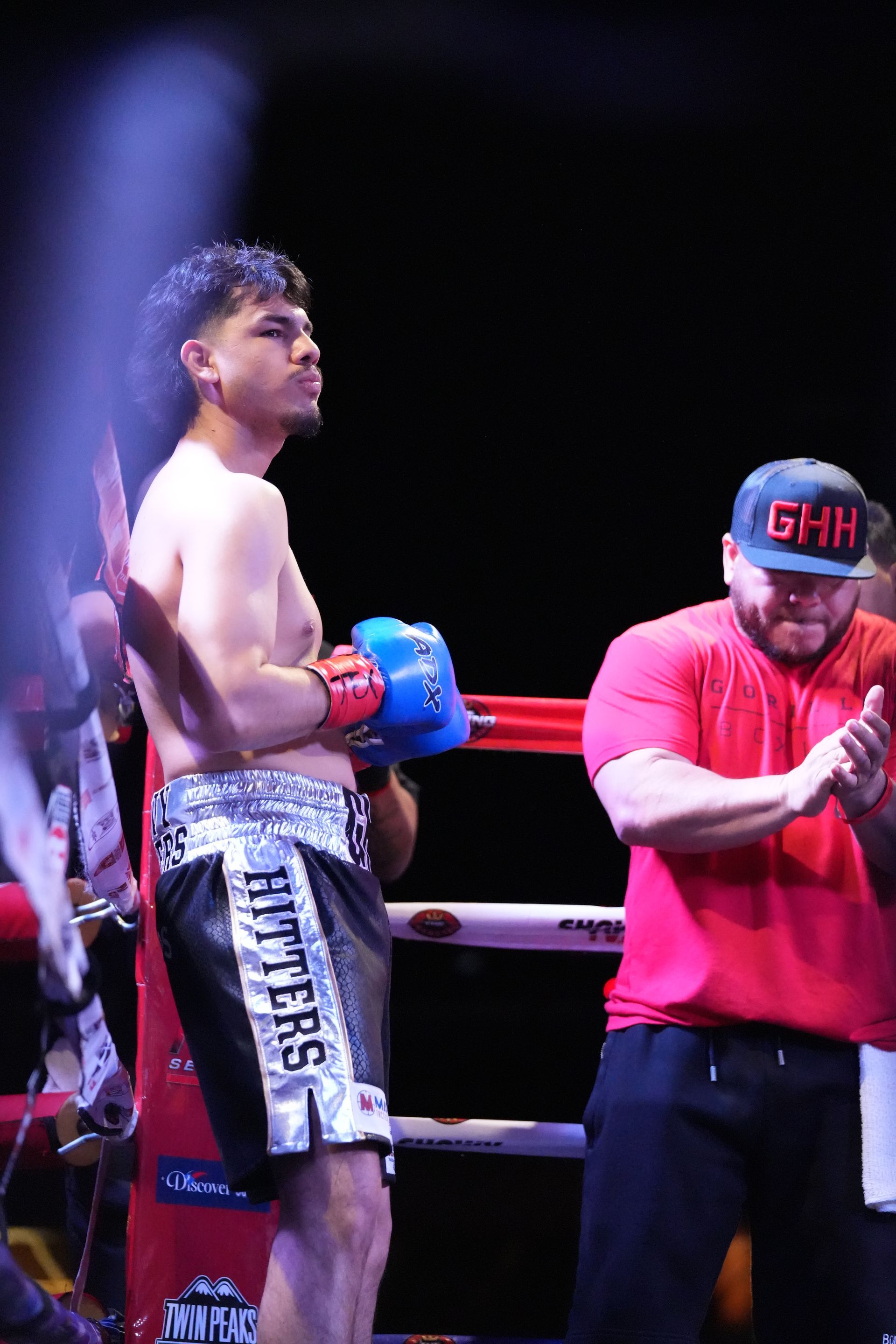 Boxer in blue gloves standing in ring beside referee in red shirt and cap