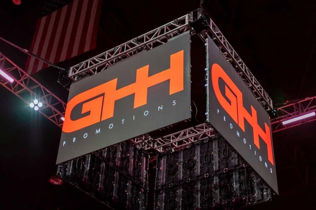 H&H Solutions logo on a hanging black cube display with orange lettering at an indoor event