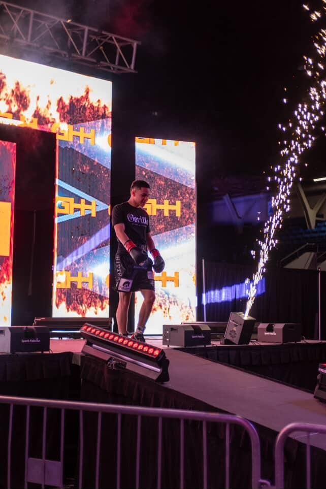 Singer on an outdoor stage with pyrotechnics and bright LED screens behind them