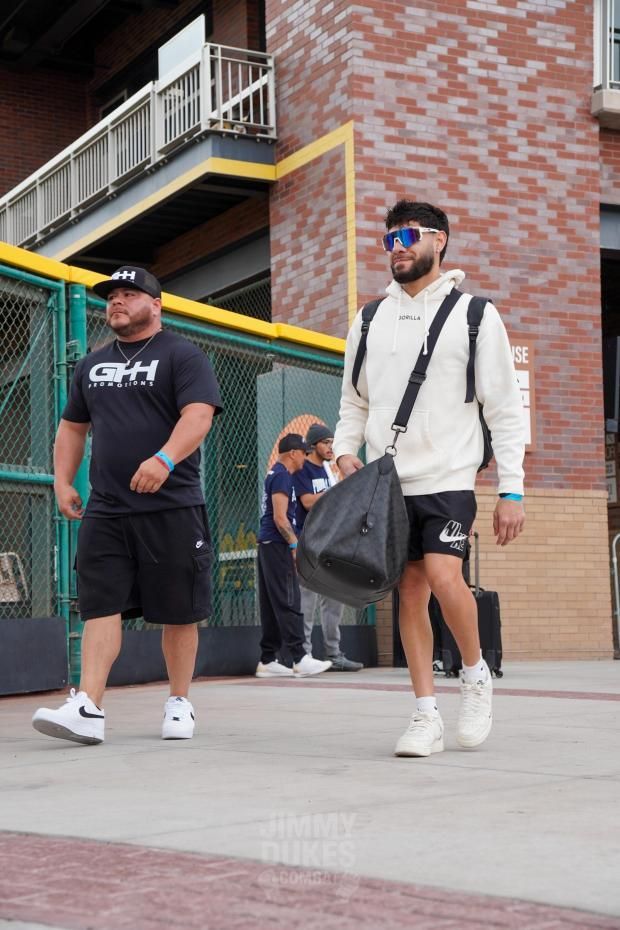 Two men walking outside a brick building, one carrying a black duffel bag.