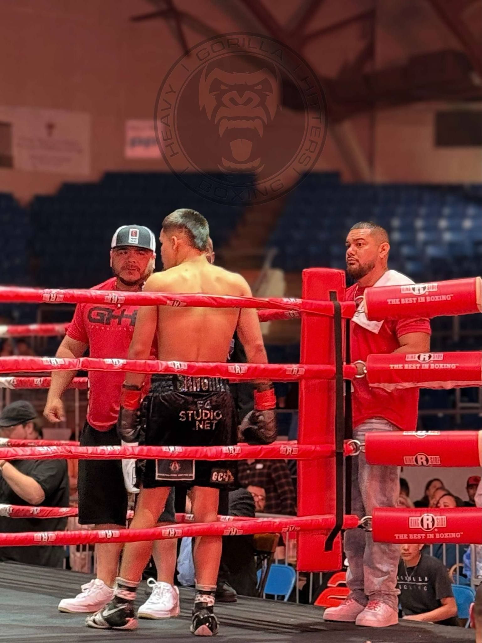 Three boxers and a referee stand in a red boxing ring after a match.