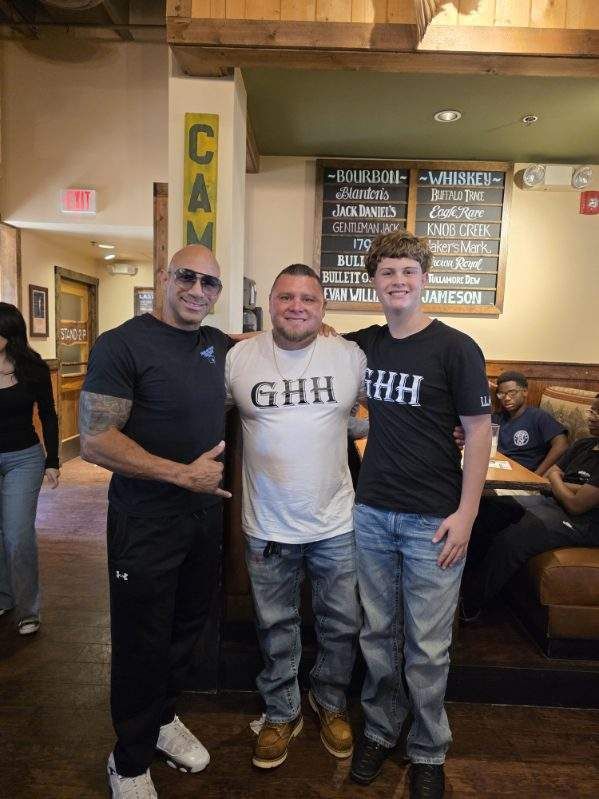 Three men standing together in a restaurant, smiling in casual T-shirts and jeans.