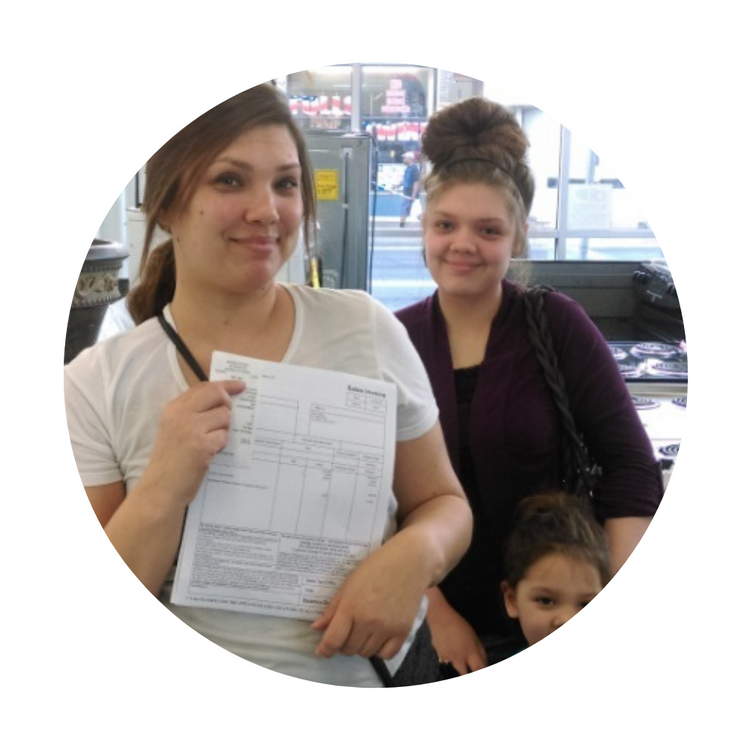 Two women and a child in an office, one woman holding paperwork and smiling at the camera.