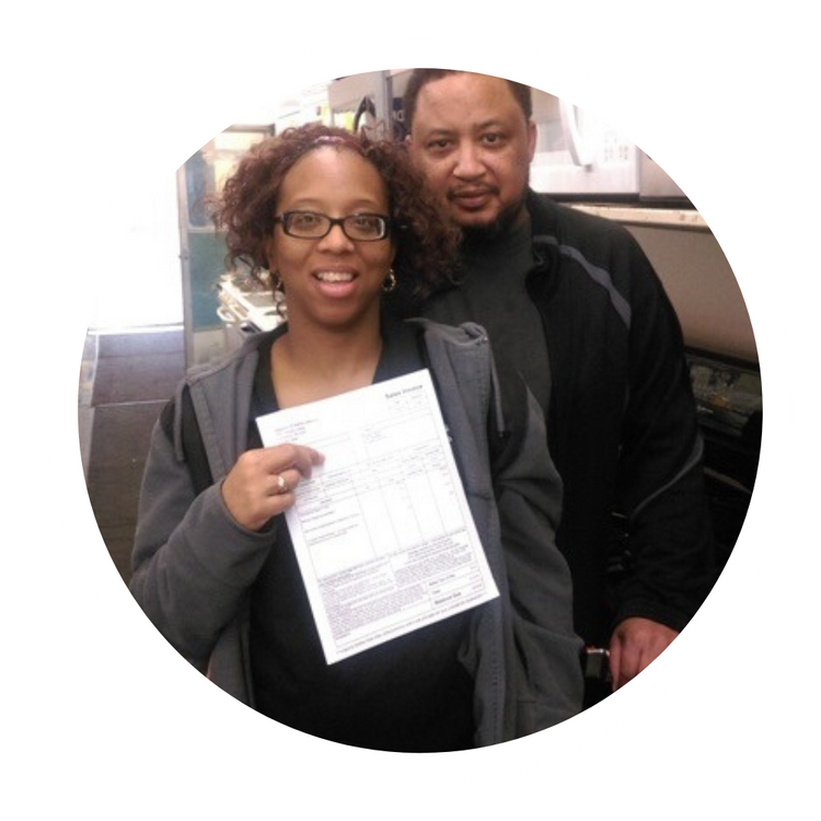 Two people smiling indoors, one holding up a document toward the camera.