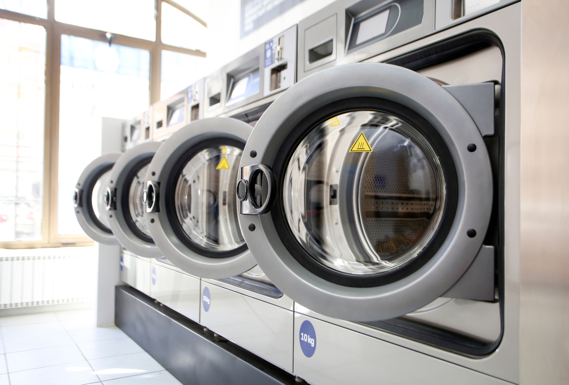 Row of commercial washing machines, silver metal with glass doors in a laundromat.