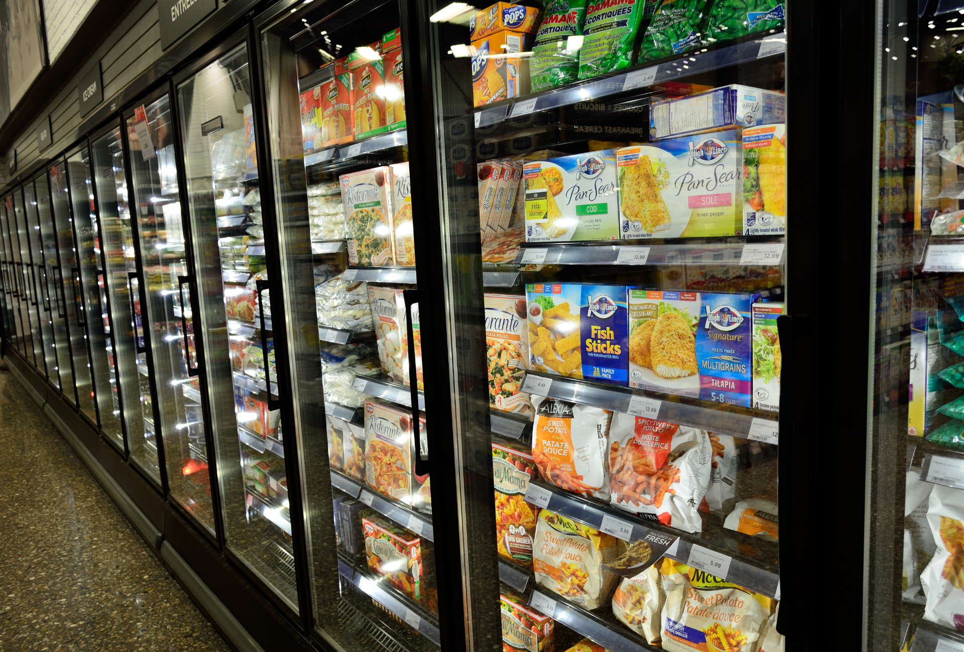 Freezer aisle in a grocery store, displaying various frozen food items behind glass doors.