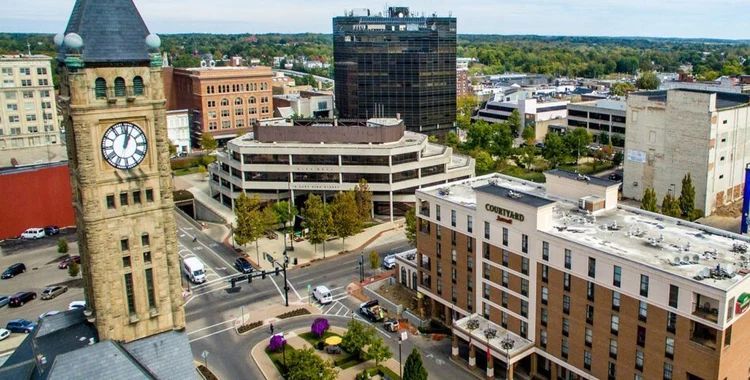 Downtown cityscape with a stone clock tower, modern buildings, and a busy street intersection