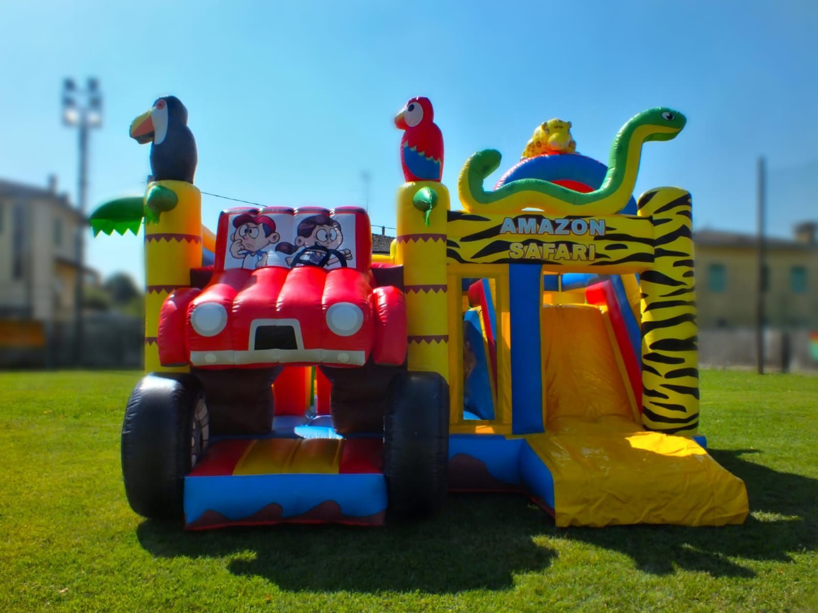 Un coloratissimo castello gonfiabile con una jeep rossa e personaggi di animali dei cartoni animati su un prato soleggiato.