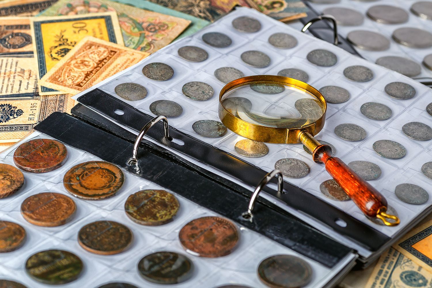 Gold coin dealer examining rare coins album with magnifying glass and vintage currency notes. Gold coin dealer examining rare coins album with magnifying glass and vintage currency notes.