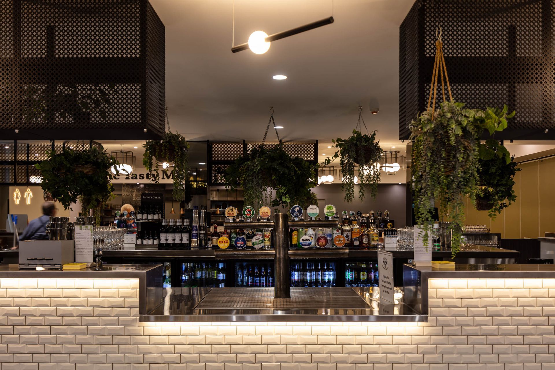 Modern café counter with hanging plants, warm lighting, and a white brick front panel