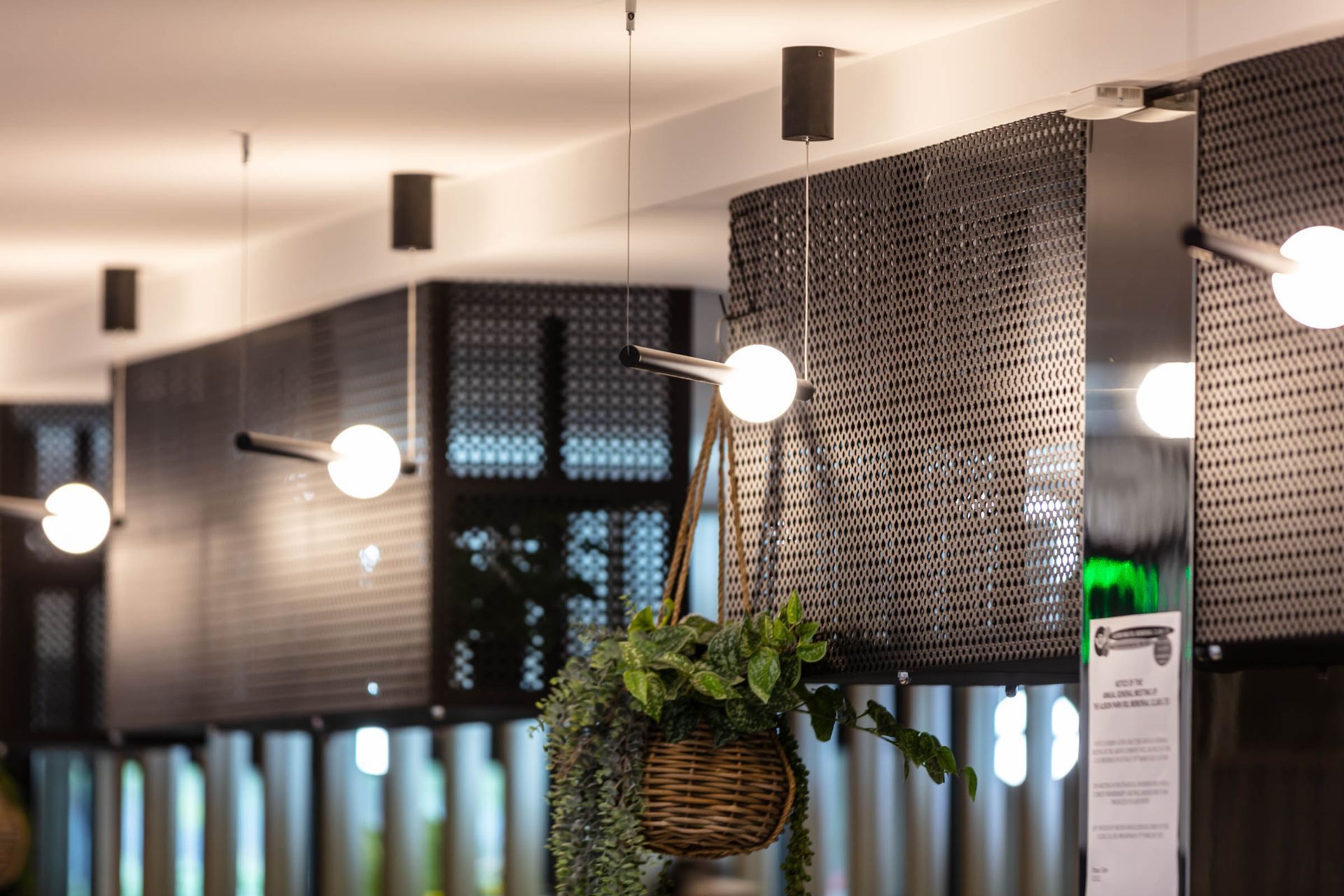 Modern café interior with hanging lights, woven wall panels, and a potted plant