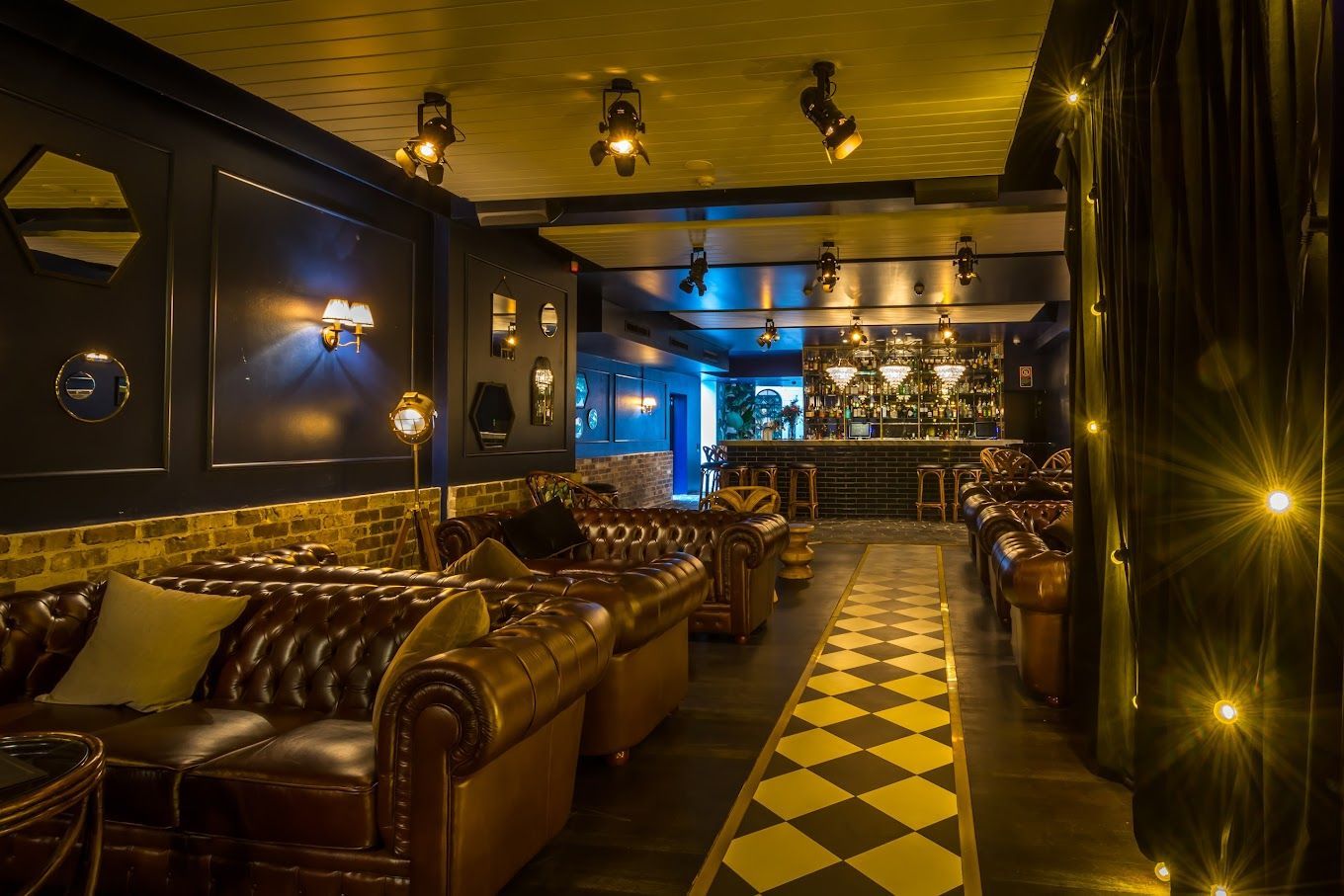 Dimly lit lounge with leather sofas, patterned floor, and warm gold lighting