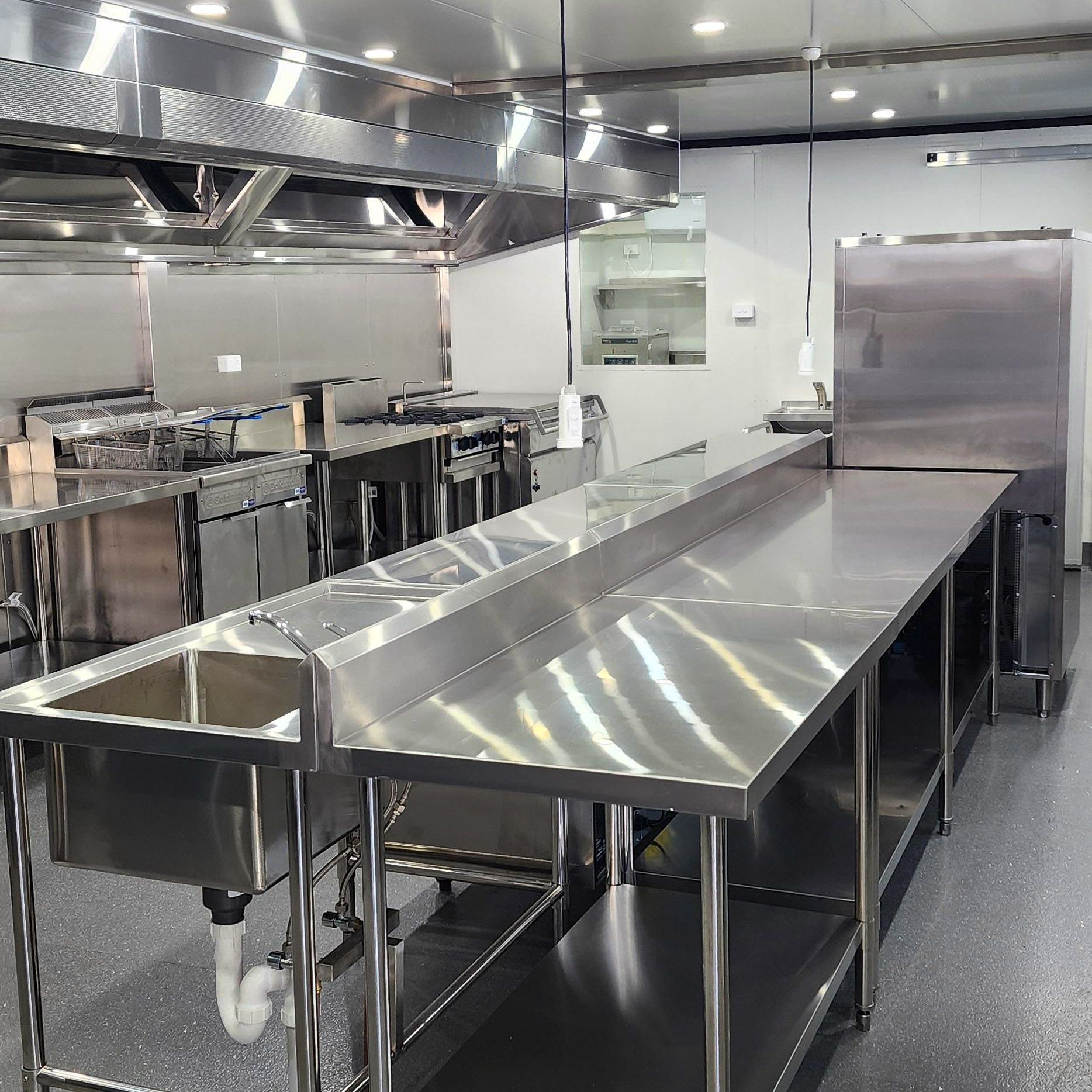 Stainless steel commercial kitchen prep tables and sink in a clean, empty workspace