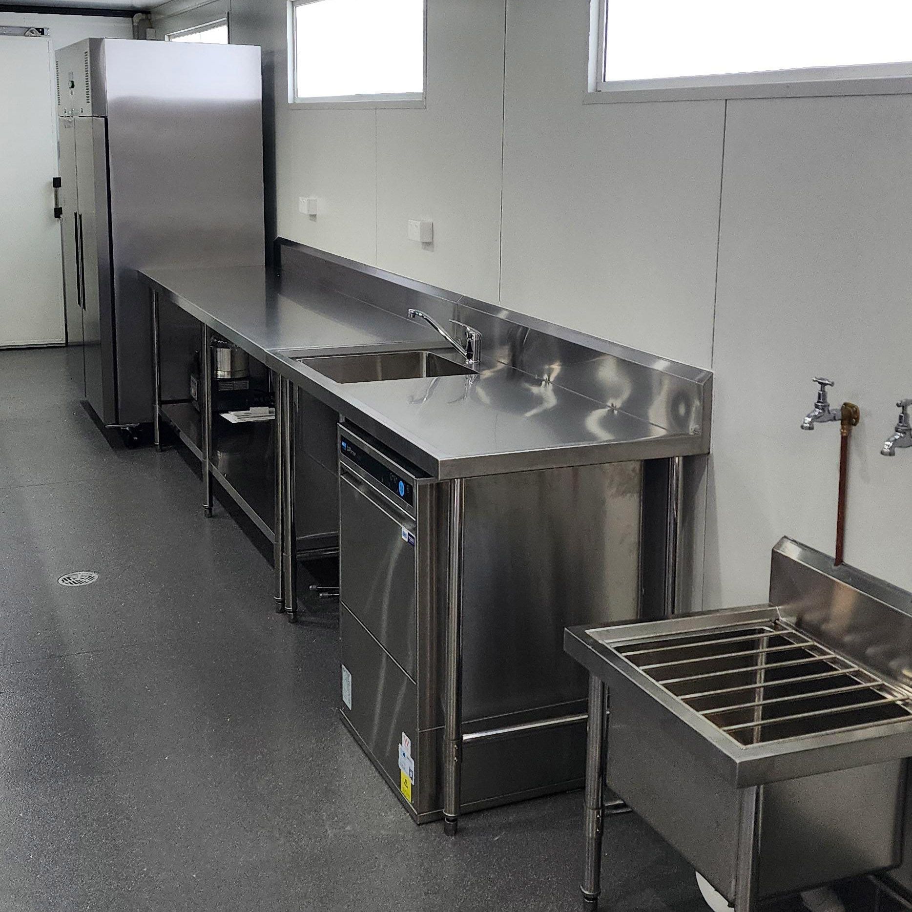 Stainless steel commercial kitchen prep area with counters, sink, dishwasher, and storage rack