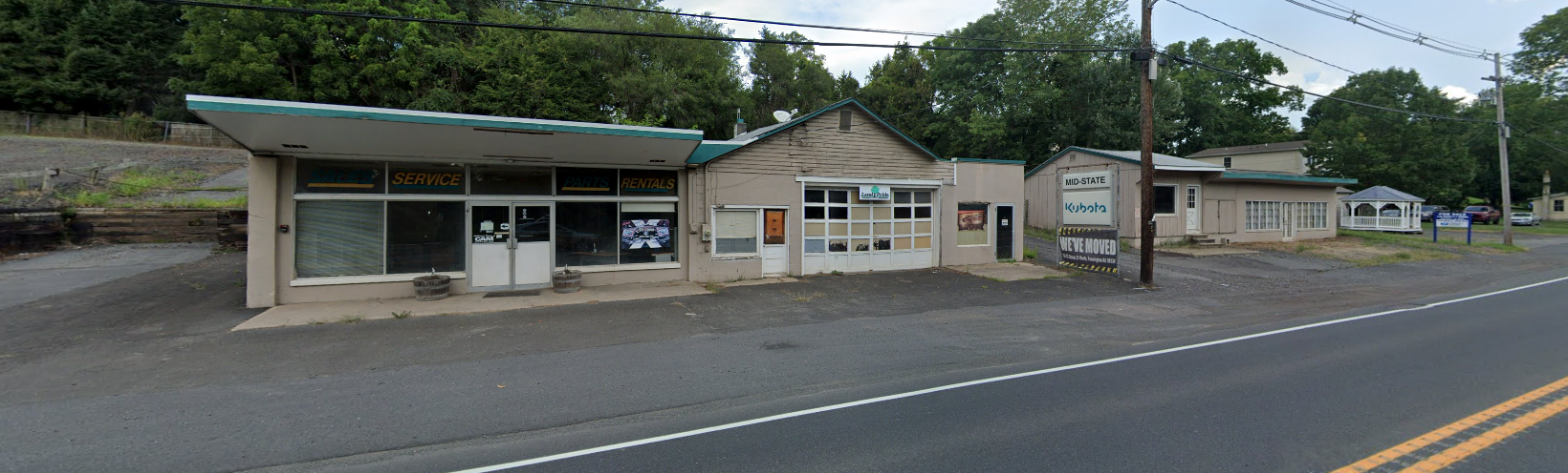 Small roadside buildings with storefronts along a quiet street, under overcast skies.