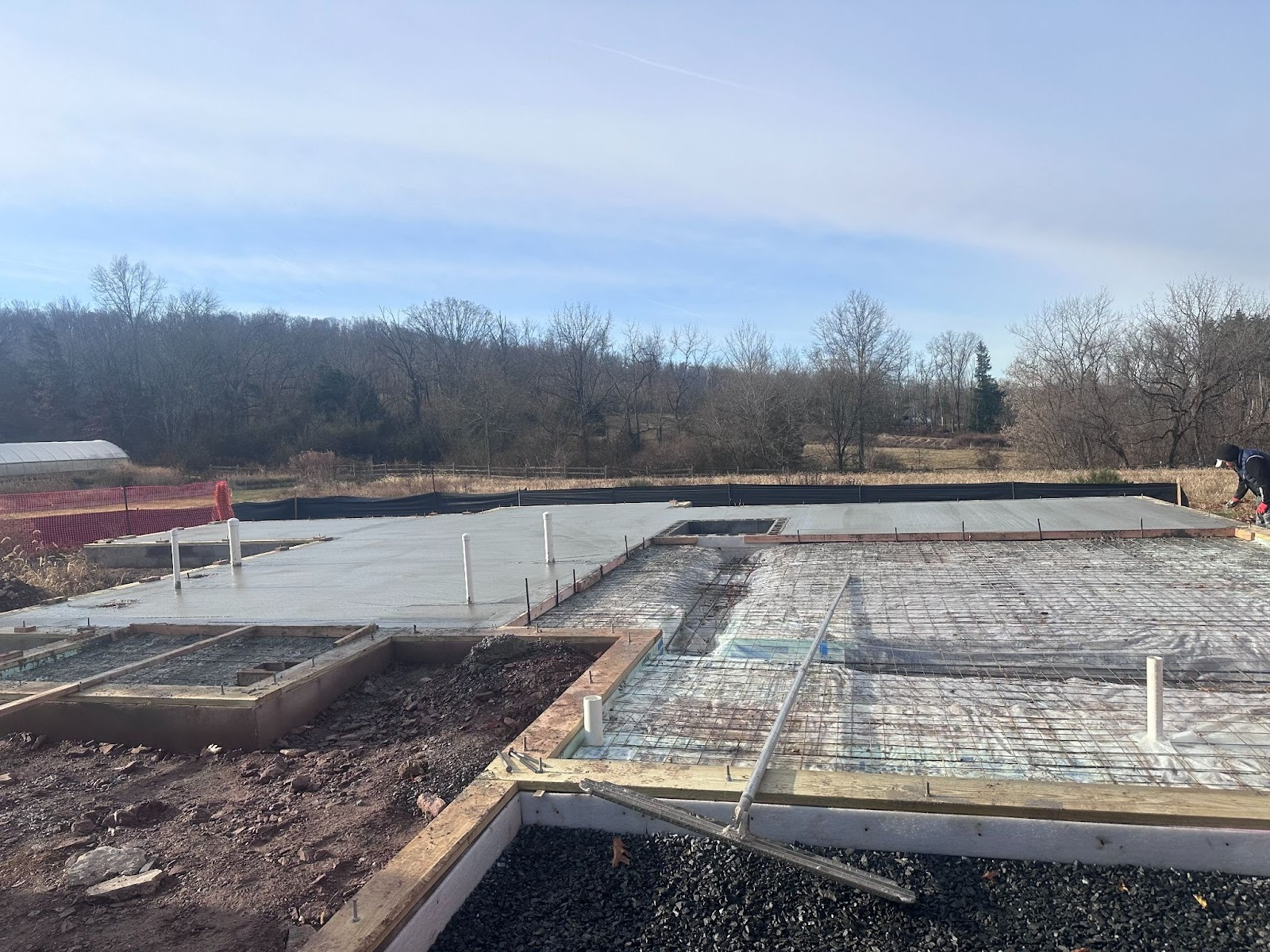 Foundation under construction with concrete slabs, rebar, and wooded background under a clear sky