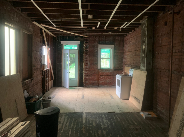 Abandoned room under renovation with exposed brick walls, unfinished ceiling, and a door to the outside
